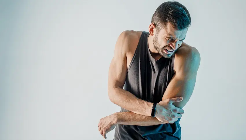 A man in athletic wear is grimacing and holding his injured elbow and needs health insurance coverage for medical treatment in Atlanta.