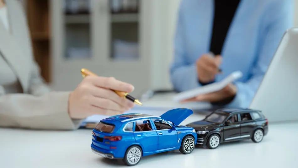 An insurance adjuster is writing notes with toy car accident models on the desk during the claim assessment and documentation process at the Atlanta Accident Lawyers office in the Atlanta Metro area.