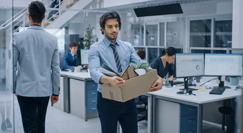 A nicely dressed man is holding a box and is leaving the workplace after termination for missing workdays following a car accident in the Atlanta Metro area.