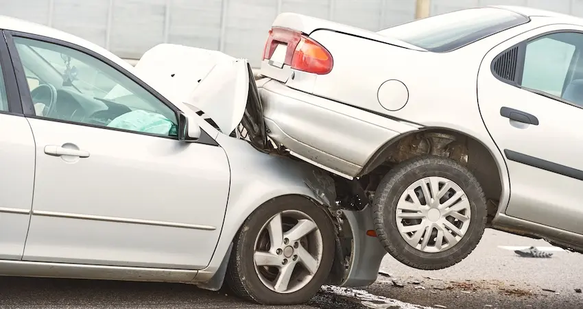 A silver car is wedged underneath the rear end of another vehicle during a violent multi-car pileup on a road, depicting the type of high-impact collision that causes serious car accident injuries requiring immediate medical attention and legal representation from Atlanta Metro Lawyers in Metro Atlanta.