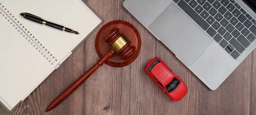 A wooden judge's gavel resting beside a red toy car- open spiral notebook- fountain pen- and laptop on a wood grain desk- symbolizing the legal steps car accident victims must take when police never showed up to file an official accident report with help from Atlanta Accident Lawyers.