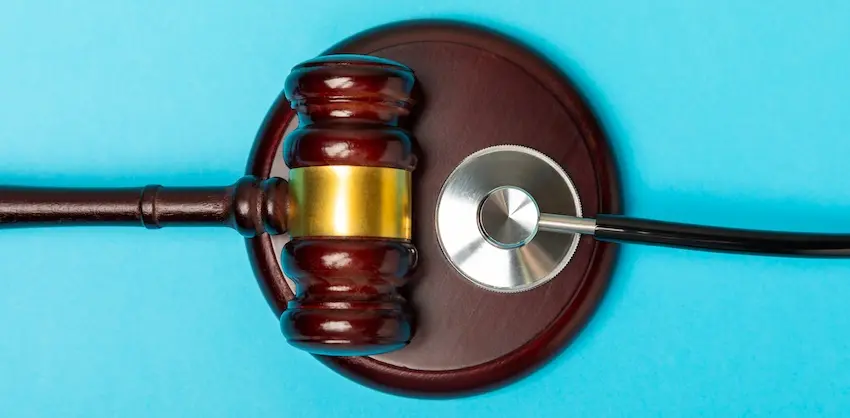 A wooden judge's gavel with a gold band rests on its sound block beside a stethoscope against a bright teal background representing the intersection of medical treatment and legal action that follows a serious back injury claim at Atlanta Accident Lawyers.