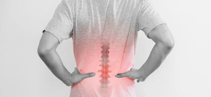 A rear view of a man pressing both hands into his lower back with a red-highlighted overlay of the spine indicating the precise area of pain providing a medical visualization of the spinal damage associated with a serious back injury in Metro Atlanta.