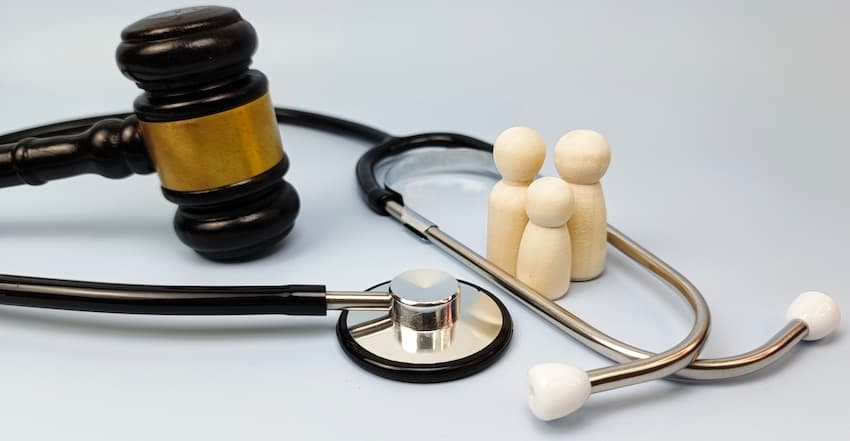 A dark wooden judge's gavel and a black stethoscope are arranged around three small wooden figurines on a white surface representing the intersection of legal and medical concerns when accident victims seek compensation to cover future medical treatments with help from Atlanta Accident Lawyers as part of a personal injury case in Metro Atlanta.