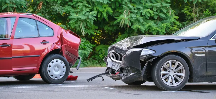 A red sedan with a crushed rear quarter panel and a black car with a heavily damaged front bumper and grille sit close together on a tree-lined road after a rear-end collision depicting the type of two-vehicle crash where each driver disputes fault and liability must be established through evidence and investigation Metro Atlanta.
